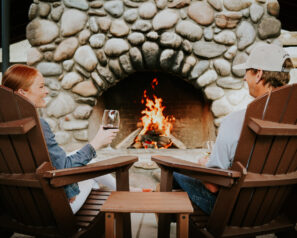 People drinking wine while sitting in front of a large stone fireplace