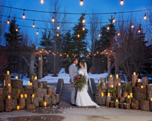 Bride and groom standing outside below string lights, surrounded by candles