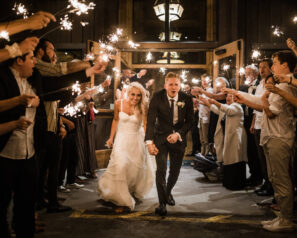 Bride and groom leaving the wedding while onlookers cheer and wave sparklers