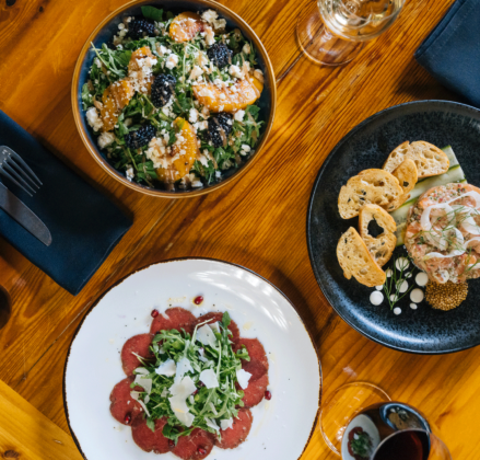 Overhead view of three delicious dishes, with place settings and wine