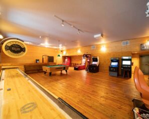 A large game room featuring a pool table, shuffle board, ski ball and several other arcade games