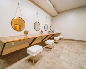 a long dressing table with four white fur stools and four large round mirrors hanging from the wall